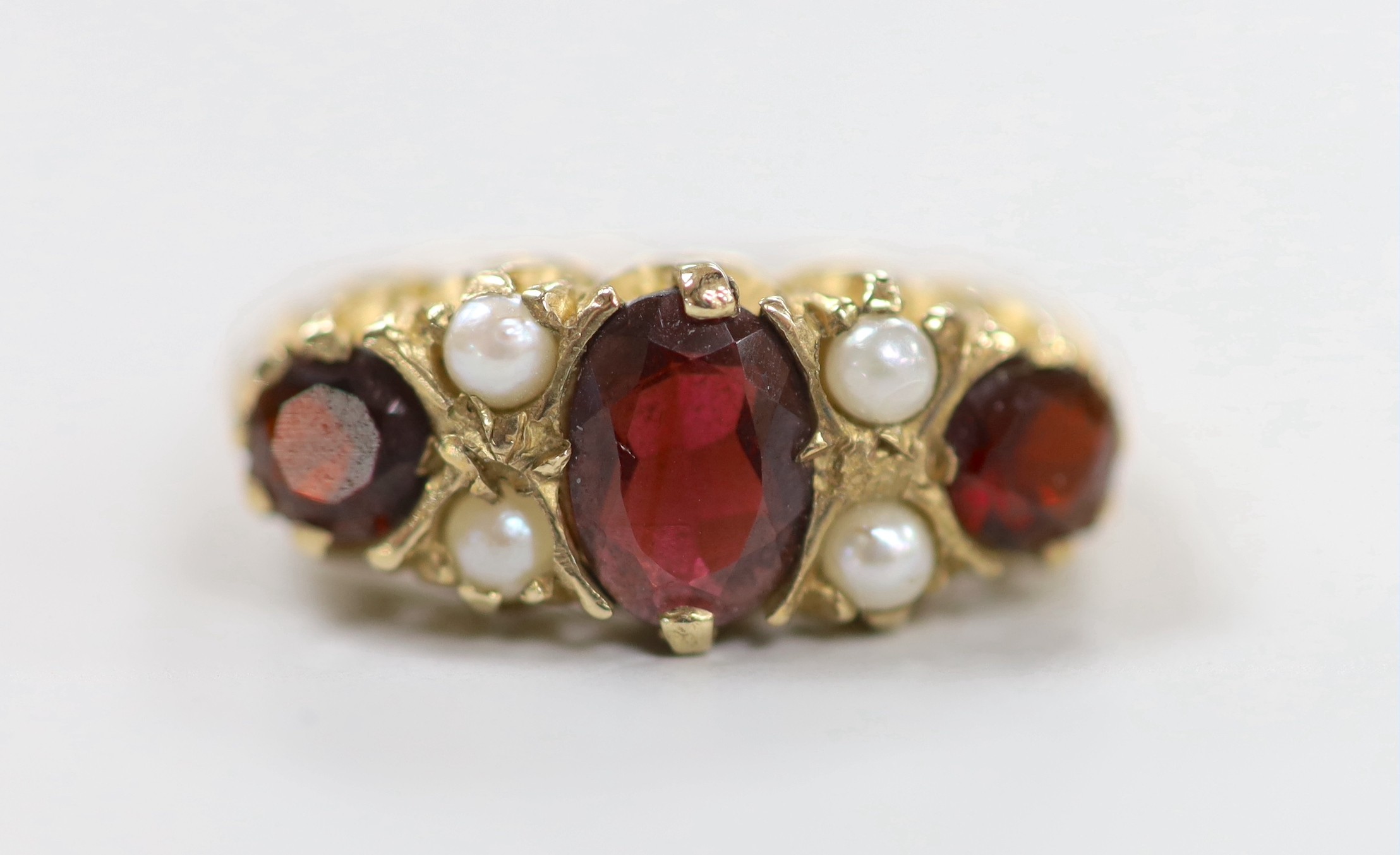 A 1970's 9ct gold, three stone garnet and four stone split pearl set half hoop ring, size K/L, gross weight 3.6 grams.